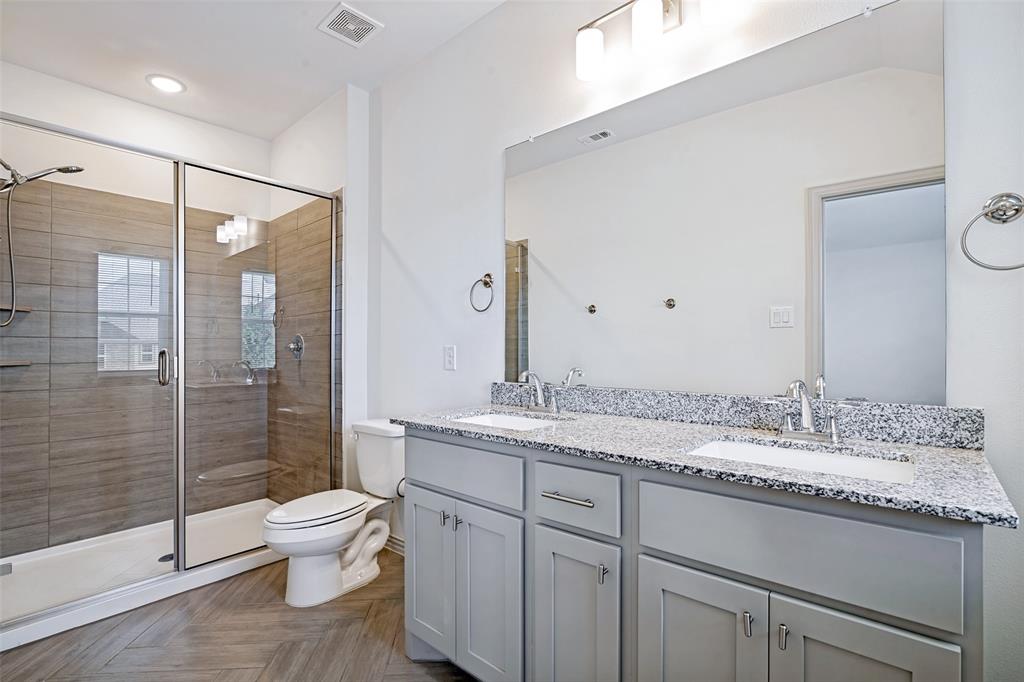 Contemporary bathroom featuring a spacious glass-enclosed shower with horizontal tile work, a dual vanity with light gray cabinetry, and a speckled countertop