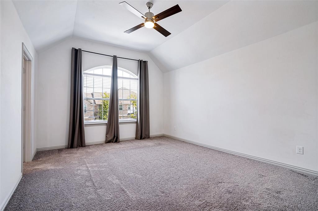 Spacious room featuring vaulted ceilings, a large arched window with blinds, a ceiling fan, and carpeted flooring