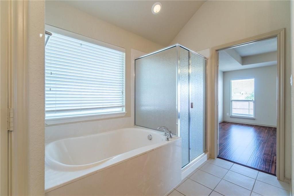 Bathroom featuring a built-in soaking tub, a frosted glass shower enclosure, and white tile flooring