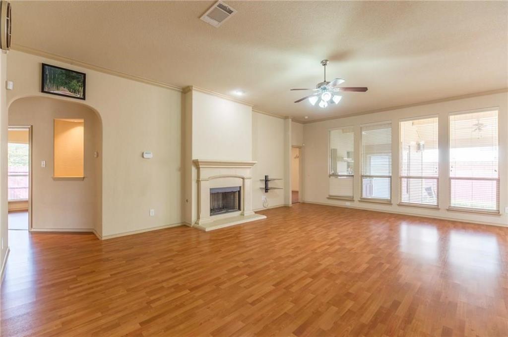 Open living area featuring wood-finish flooring, a decorative fireplace with a mantel, and a ceiling fan