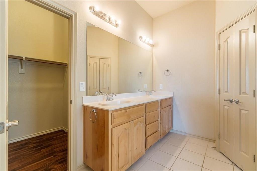 Bathroom featuring a double vanity with wood-finish cabinetry and light-colored countertops, dual sinks with chrome fixtures, and a large wall-mounted mirror
