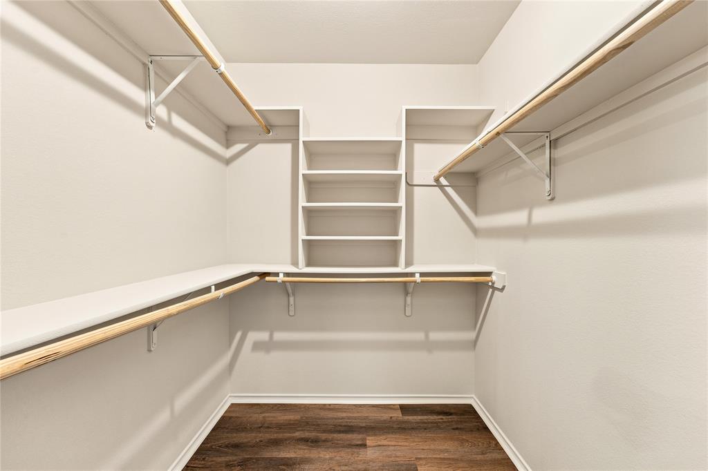 Walk-in closet featuring wood-finish flooring, white shelving, and multiple clothing rods