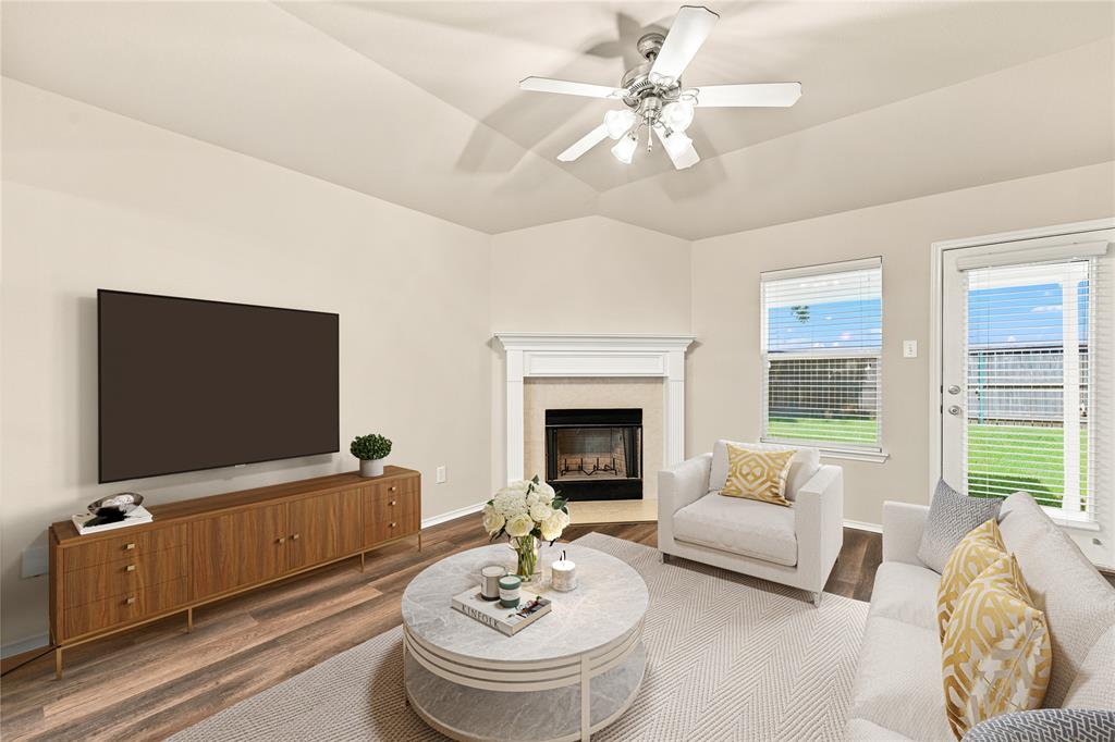 Living area featuring wood-finish flooring, a tray ceiling with a ceiling fan, and a corner fireplace with a white mantel