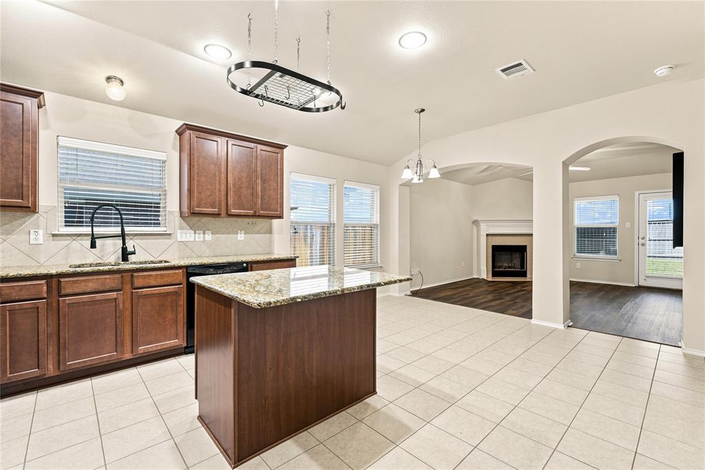 Kitchen featuring a central island, wood-finish cabinetry, granite countertops, and a tile backsplash