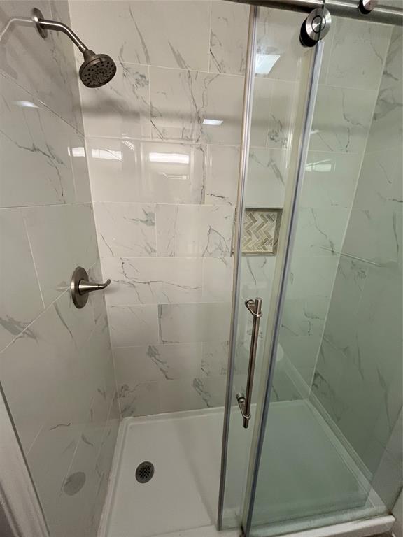 Shower enclosure featuring white marble-look subway tile, a recessed niche with herringbone pattern accent tile, a sliding glass door, a white shower pan, and brushed nickel fixtures