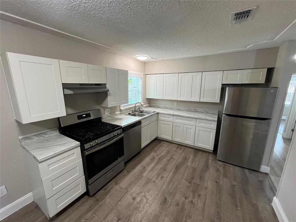 Modern kitchen featuring a gas range, stainless steel appliances, white shaker cabinetry, wood-finish flooring, and light-toned countertops