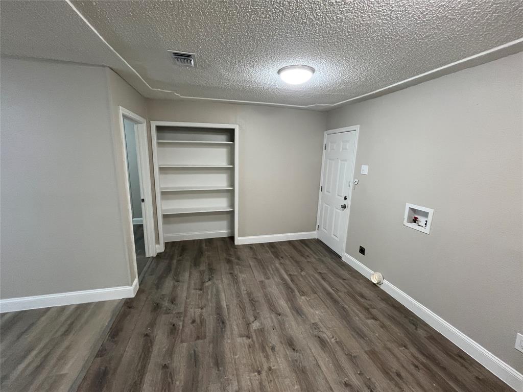 Room featuring neutral wall paint, wood-finish flooring, built-in shelving, a paneled door, and a utility hookup