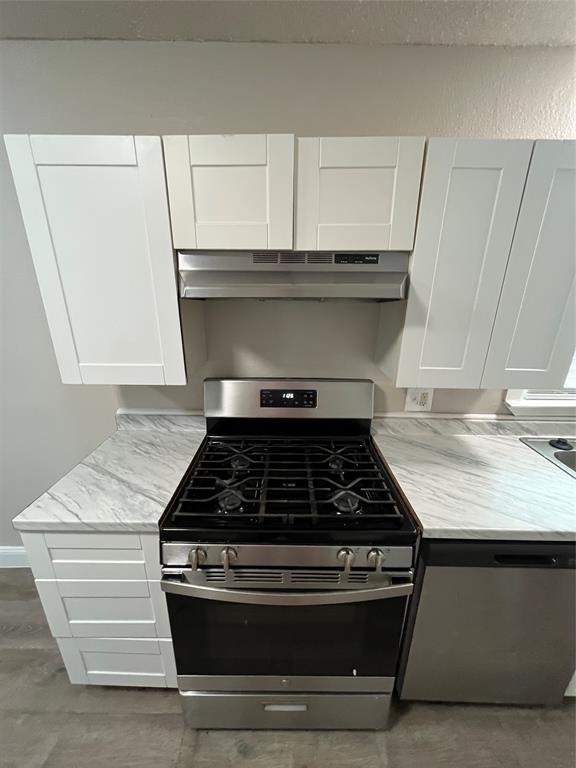 Stainless steel range with a gas cooktop, under-cabinet range hood, white shaker-style cabinetry, white countertops with gray veining, and wood-finish flooring
