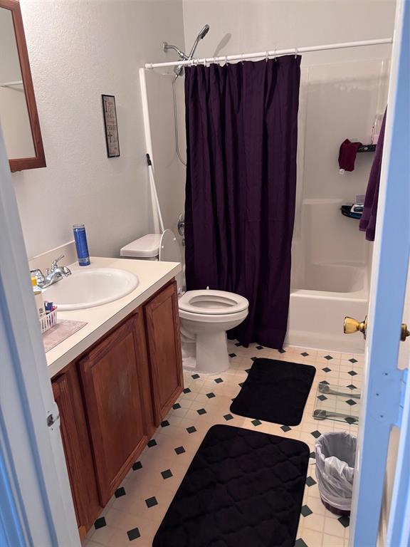 Full bathroom featuring a white tub/shower combination with a chrome shower head, a white toilet, and a vanity with wood-finish cabinetry, a white countertop, and an integrated sink with a chrome faucet