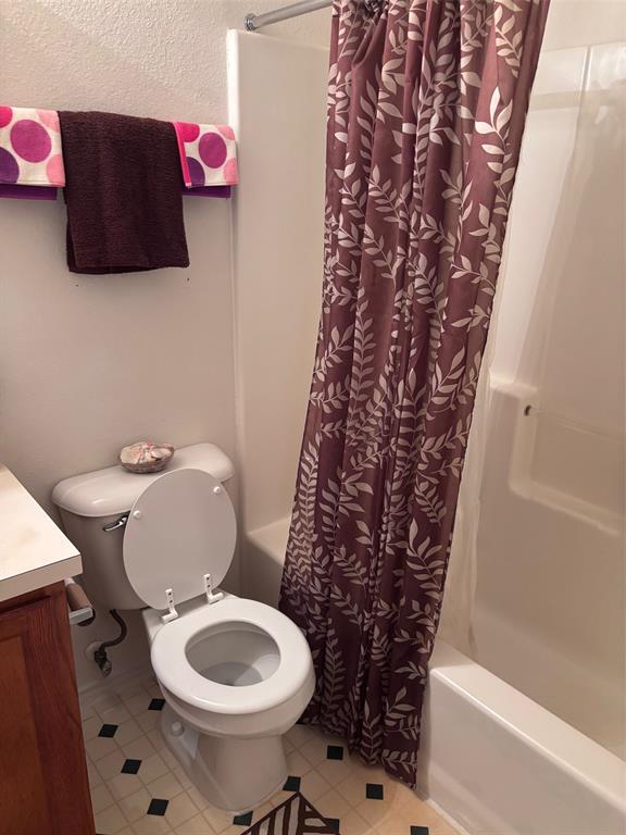 Bathroom featuring a white toilet, integrated tub and shower unit, and patterned floor tiling