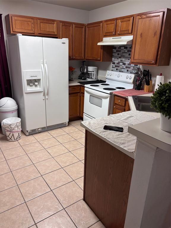 Kitchen featuring wood-finish cabinetry, tile flooring, a white side-by-side refrigerator, white range, and a mosaic tile backsplash