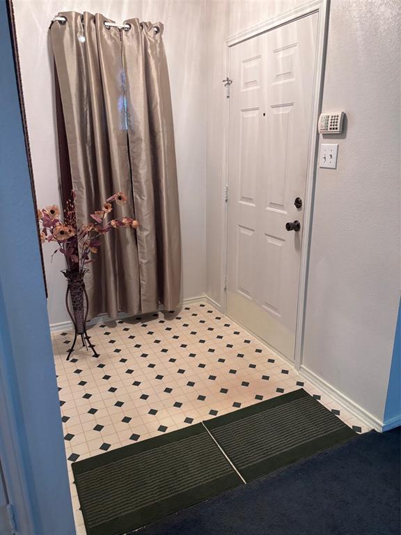 Entryway featuring a white paneled door with black hardware, patterned tile flooring, and white baseboards