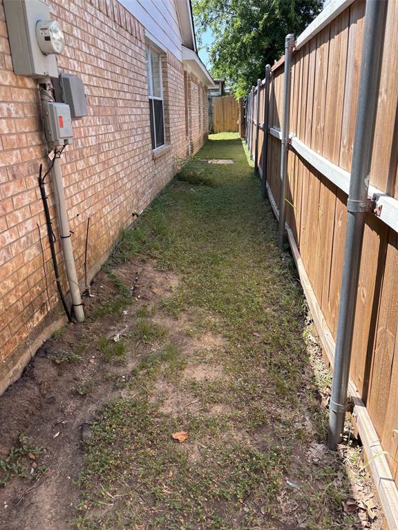 Side yard featuring a red brick exterior, multiple windows, a wooden privacy fence, and a grassy path