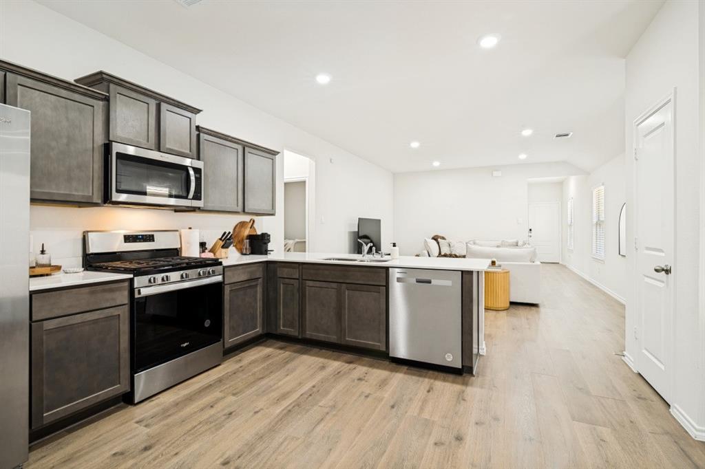 Gourmet kitchen featuring dark wood-finish cabinetry, stainless steel appliances, white countertops, and wood-finish flooring