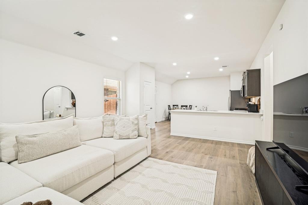 Open-concept living area with wood-finish flooring, recessed lighting, and a kitchen featuring dark cabinetry and a light-toned countertop