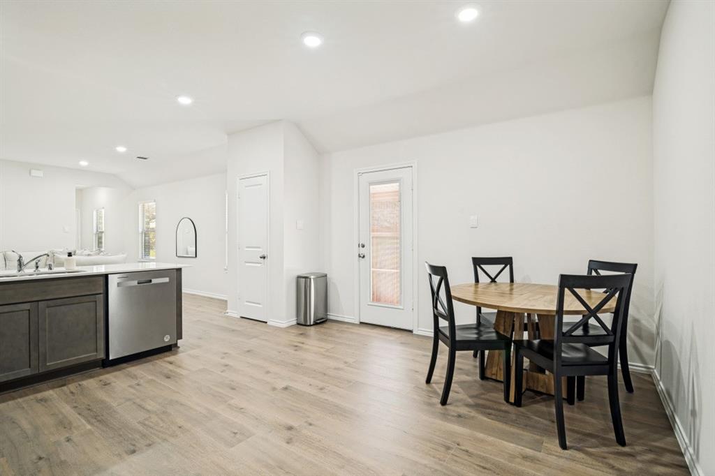 Open-concept living space with wood-finish flooring, recessed lighting, white walls, and a glass-paneled rear exit door