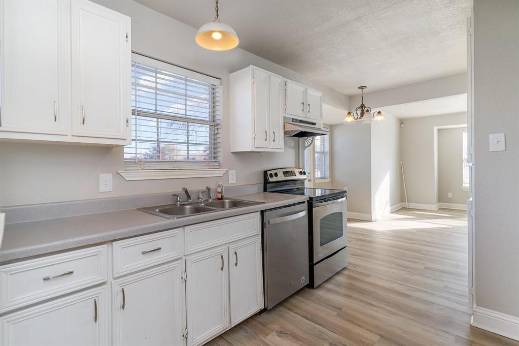 Kitchen featuring white cabinetry with silver-tone hardware, a double basin stainless steel sink, light grey countertops, and stainless steel appliances including a range and dishwasher