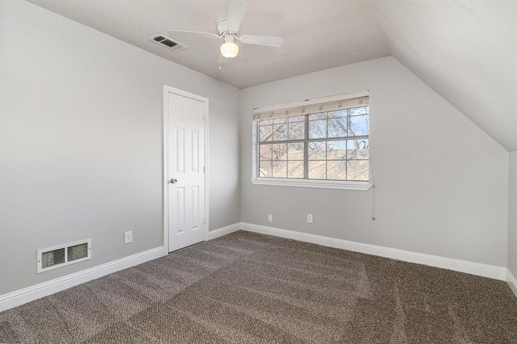 Room featuring neutral gray wall paint, textured carpeting, a multi-pane window with blinds, and an angled ceiling
