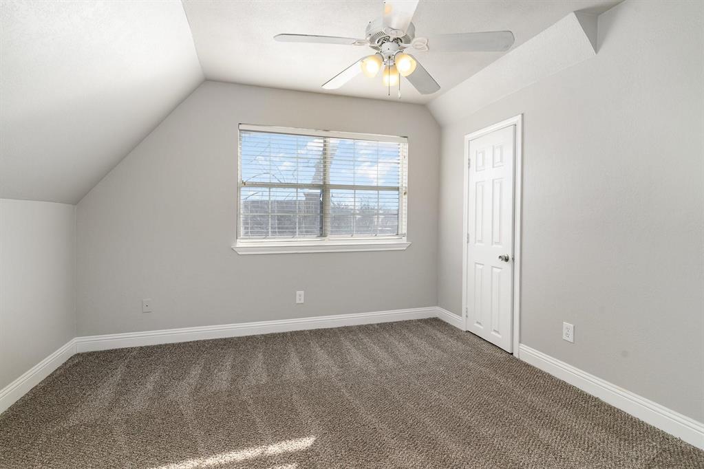 Carpeted room featuring a window with blinds, a white ceiling fan with integrated lighting, a paneled door, and angled ceilings
