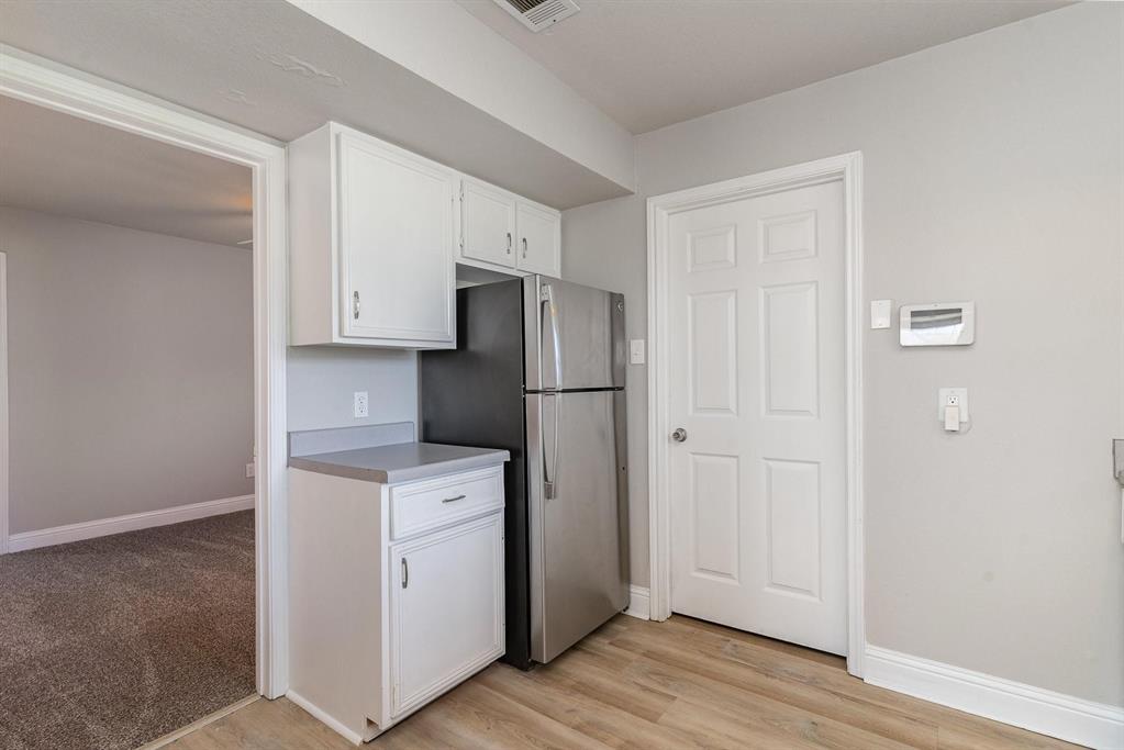 Compact kitchen area featuring white cabinetry, a light-toned countertop, and stainless steel refrigerator