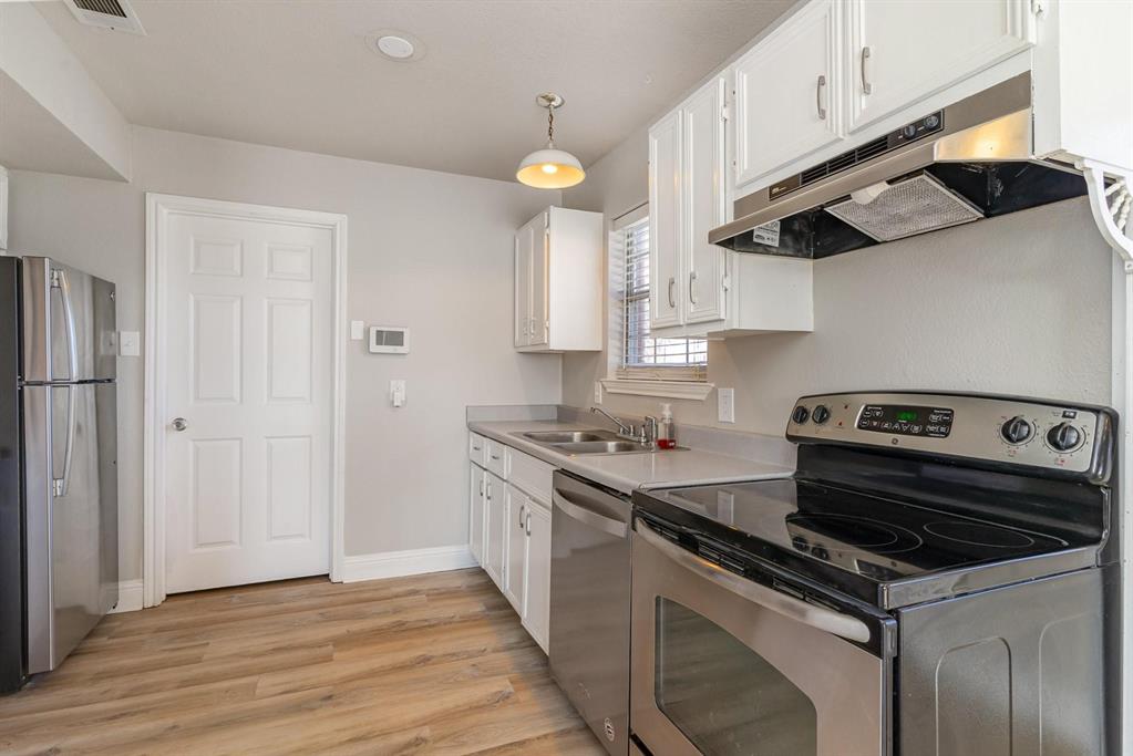 Kitchen featuring stainless steel appliances, wood-finish flooring, white cabinetry, light-toned countertops, and a window with blinds
