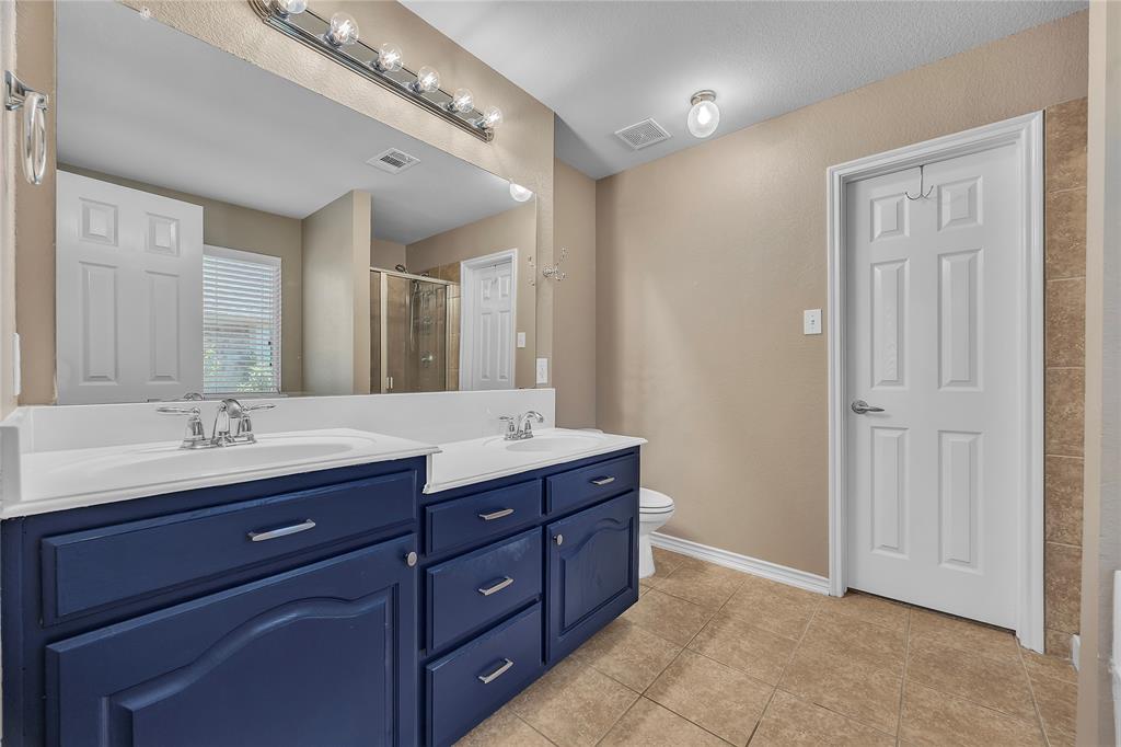 Dual vanity with integrated sinks, ample cabinet storage, a large wall-mounted mirror, overhead vanity lighting, and tile flooring
