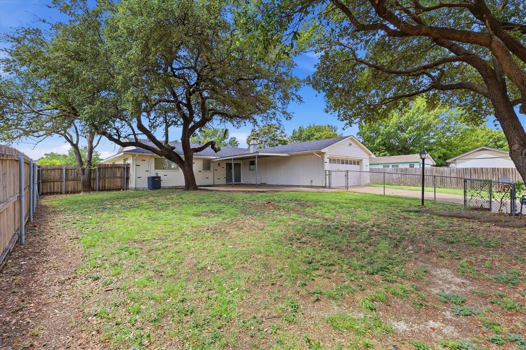 Expansive backyard featuring mature trees, a wooden privacy fence, chain-link fencing, and a concrete patio