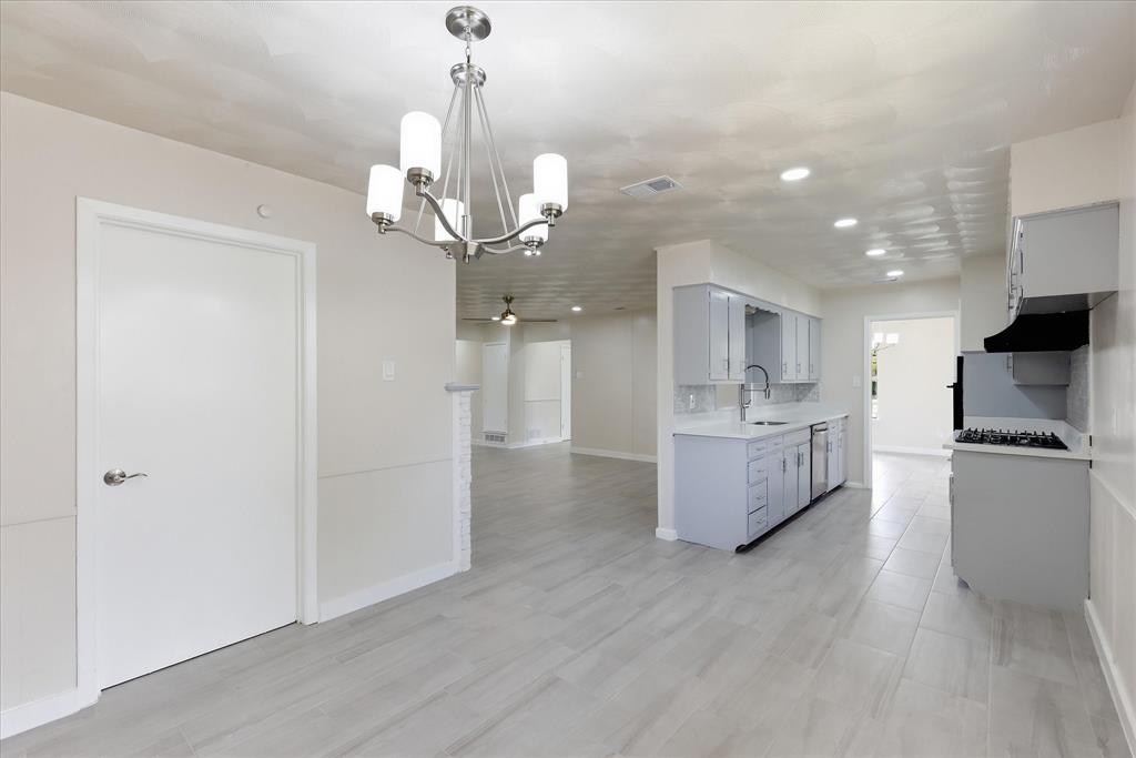 Open-concept living space featuring wood-finish flooring, a contemporary chandelier, recessed lighting, light-toned walls, and a modern kitchen with grey cabinetry and stainless steel appliances
