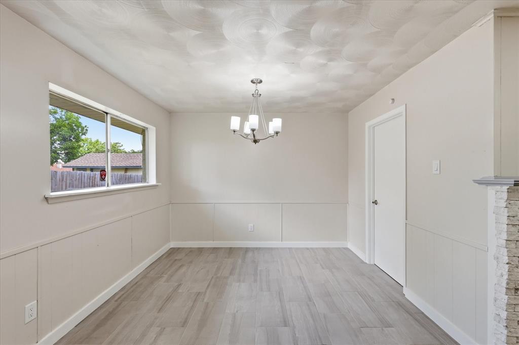 Spacious room featuring wood-finish flooring, wainscoting, and a multi-light chandelier