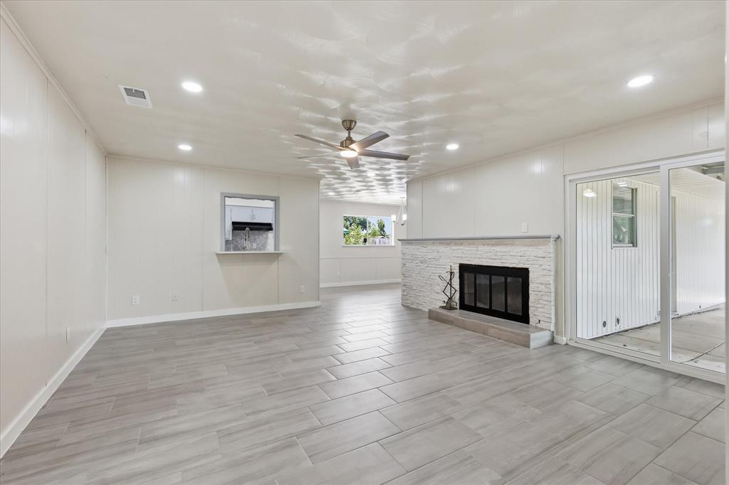 Spacious living area featuring light wood-finish flooring, a white brick fireplace with a dark firebox, a ceiling fan, recessed lighting, and a pass-through window with a lower shelf