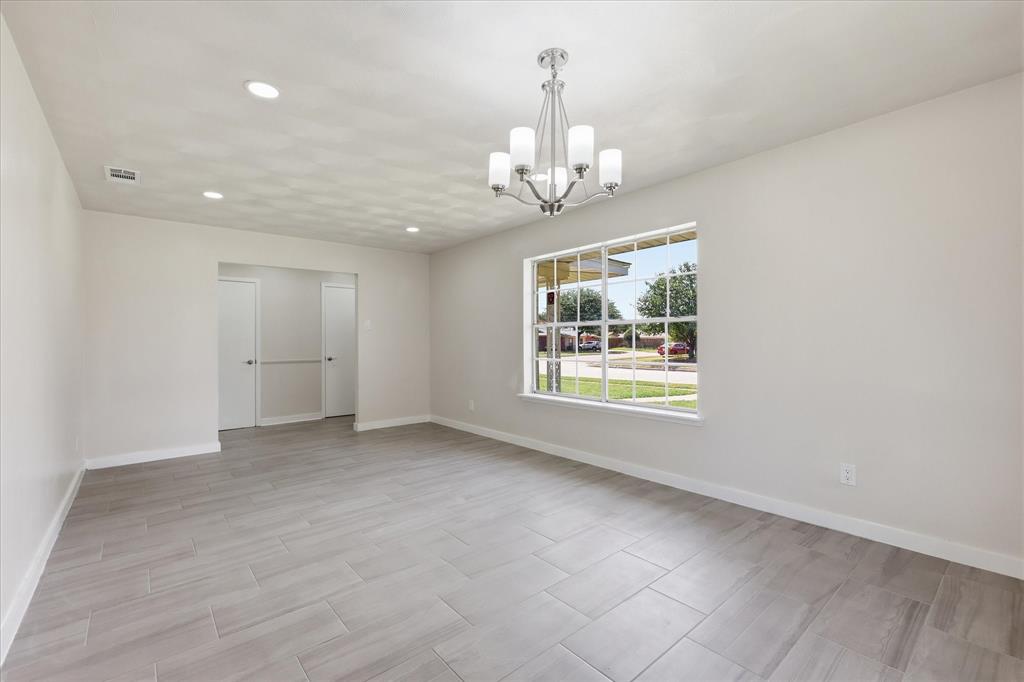 Spacious room featuring light gray walls, large front-facing window, recessed lighting, and a chrome chandelier with five frosted glass shades