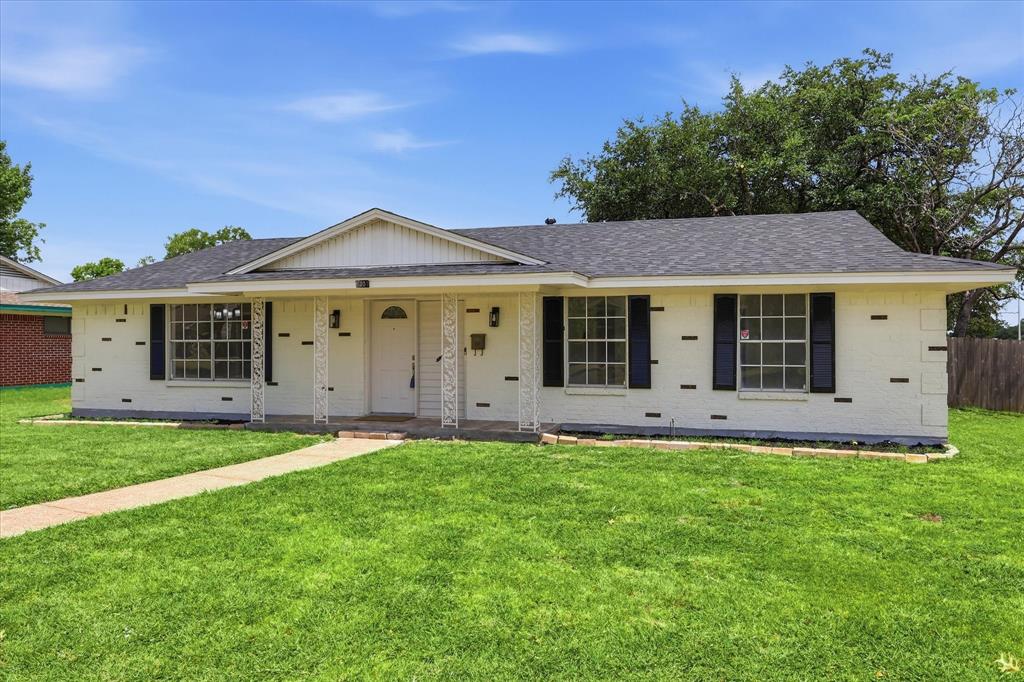 Single-story residence featuring a white brick exterior with dark trim accents, a front porch with decorative columns, a gabled entry, and a dark shingle roof