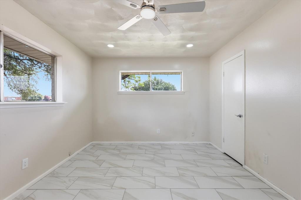 Spacious room featuring large format tile flooring, two windows, recessed lighting, a ceiling fan, and a solid door