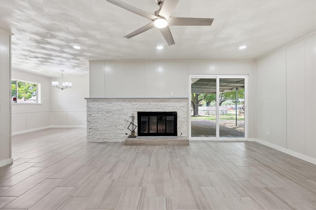 Spacious living area featuring wood-look tile flooring, a white brick fireplace with a stone mantel, recessed lighting, and a ceiling fan