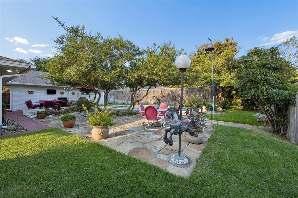 Expansive backyard featuring a stone patio, mature trees, manicured lawn, and a covered outdoor living area with a built-in entertainment system
