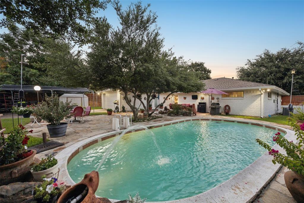 Oval-shaped swimming pool with a stone coping and water features, surrounded by a stone patio.
