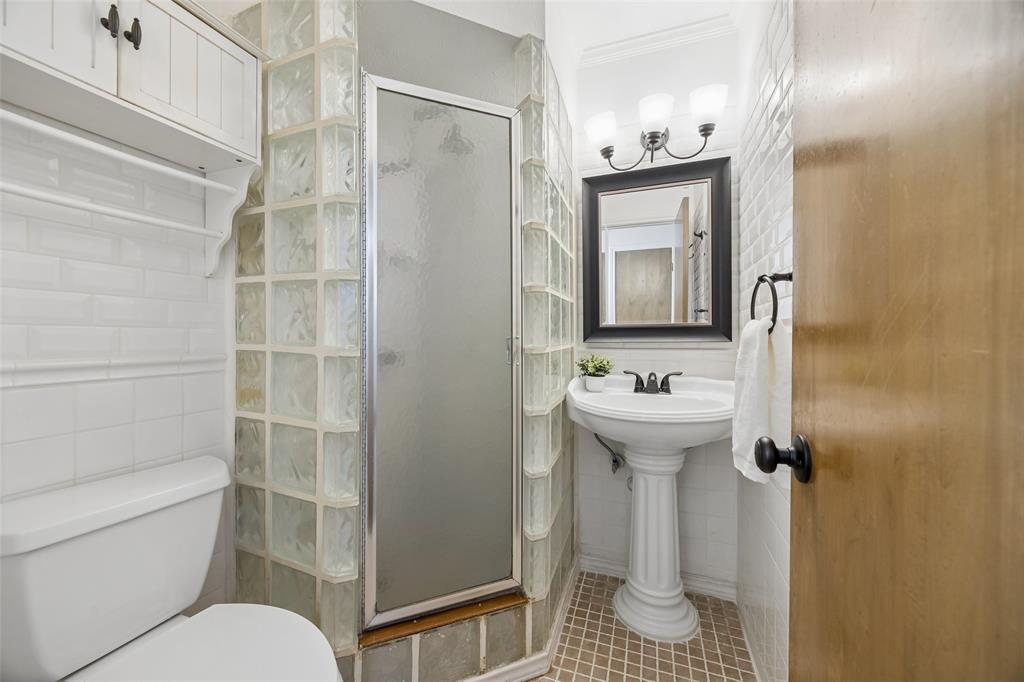 Bathroom featuring a glass block shower enclosure, white subway tile walls, and a pedestal sink with a framed mirror