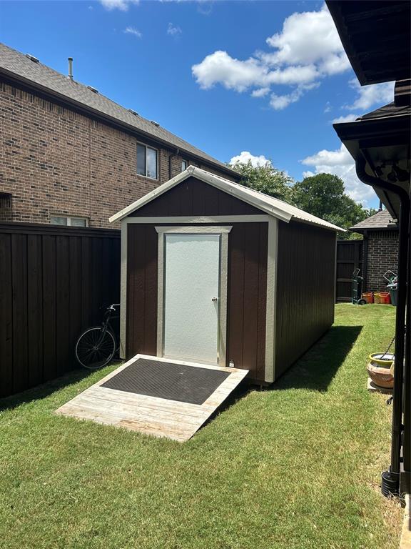 Detached storage shed with brown siding and white trim, featuring a white door, a sloped wood ramp, and a metal roof