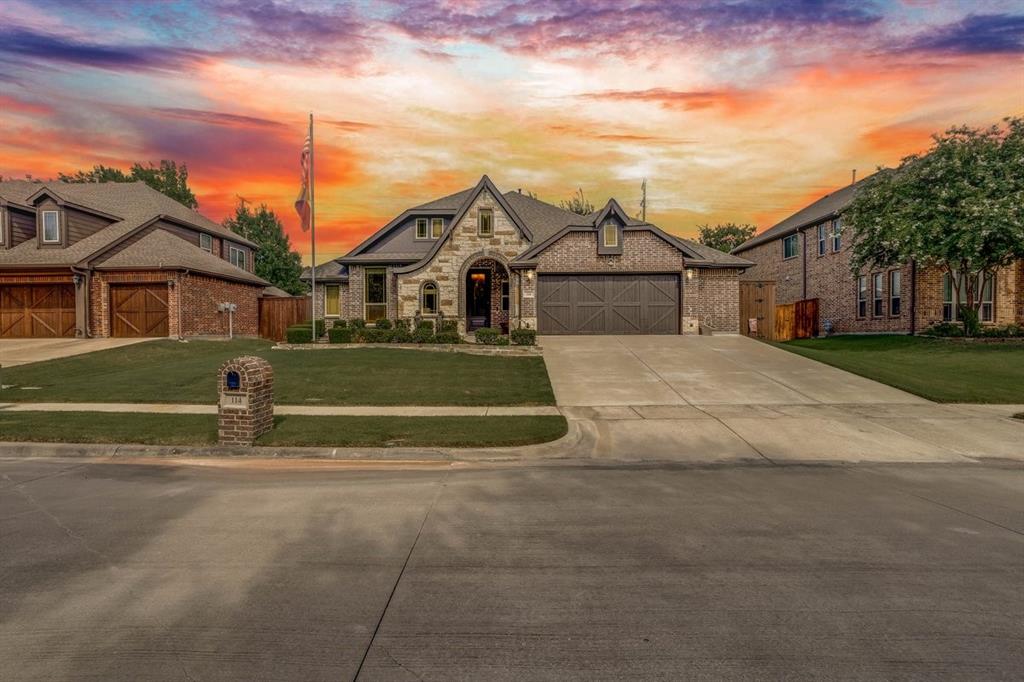 Exterior featuring a stone and brick facade, arched entry, two-car garage with a decorative door, concrete driveway, and a manicured lawn Exterior featuring a stone and brick facade, arched entry, two-car garage with a decorative door, concrete driveway, and a manicured lawn