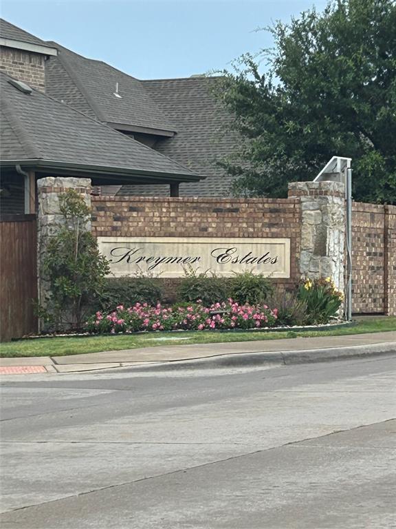 Stone and brick entryway signage featuring "Kreymer Estates" inscription, surrounded by lush landscaping and flowering pink plants