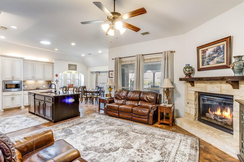 Open-concept living space featuring wood-finish flooring, a stone-surround fireplace with a wood mantel, and an overhead ceiling fan