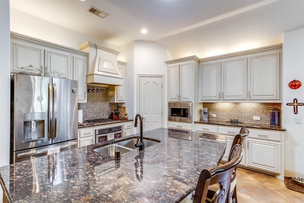 Kitchen featuring an expansive island with a dual-basin sink, under-cabinet lighting, stainless steel appliances, a decorative range hood, and light-toned cabinetry