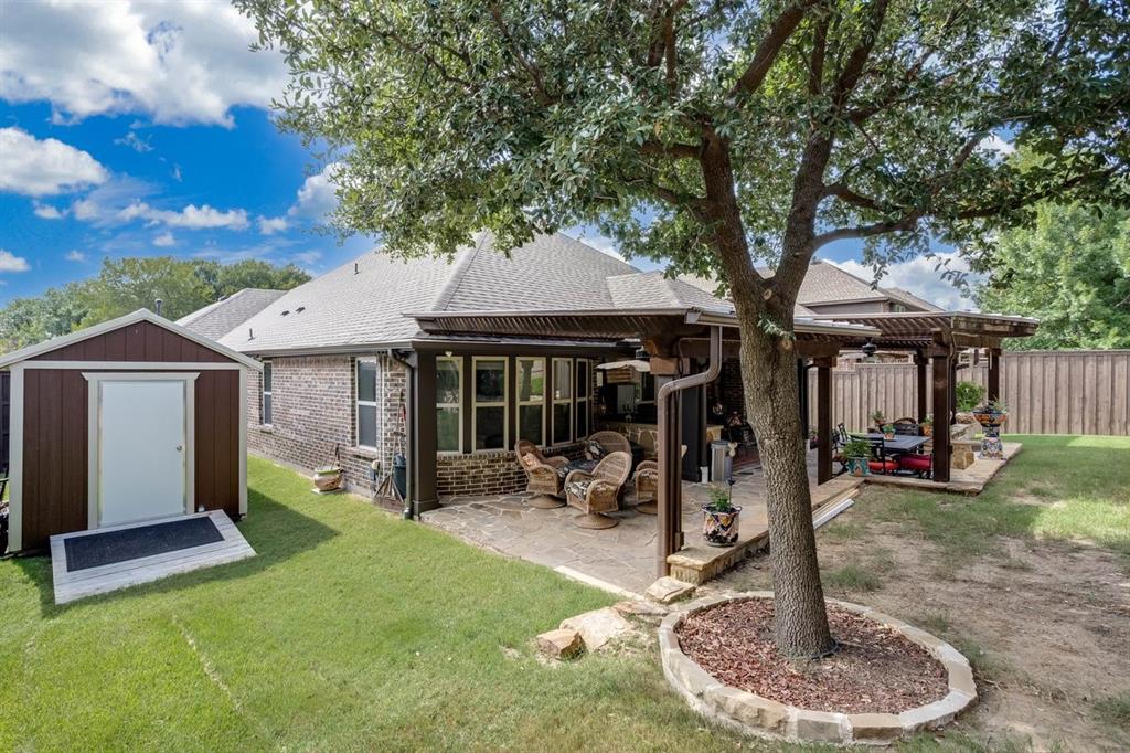 Expansive backyard featuring a stone patio, large pergola, and mature trees