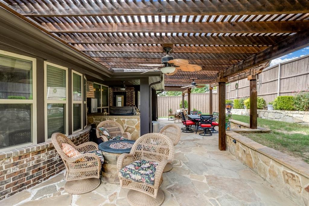 Expansive stone patio with a wood pergola, integrated ceiling fans, and a built-in fire pit