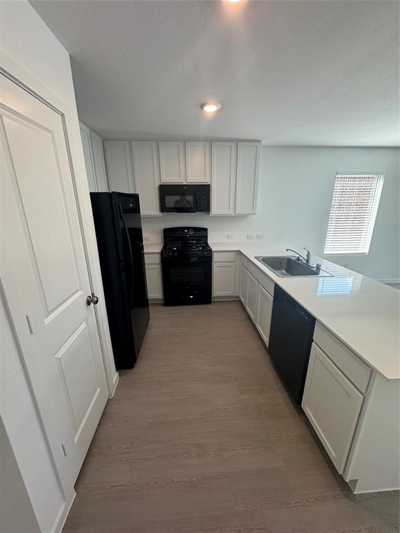 Kitchen with light countertops, a peninsula, black appliances, white cabinets, and a textured ceiling Kitchen with light countertops, a peninsula, black appliances, white cabinets, and a textured ceiling