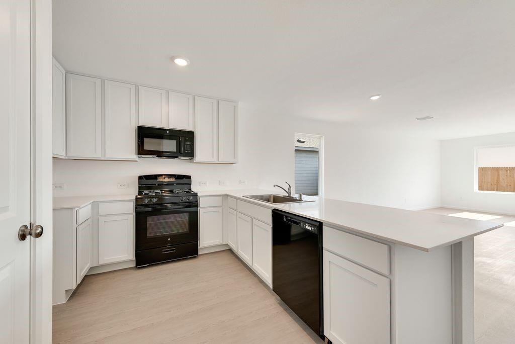 Kitchen featuring black appliances, a peninsula, light countertops, light wood-style flooring, and white cabinets Kitchen featuring black appliances, a peninsula, light countertops, light wood-style flooring, and white cabinets