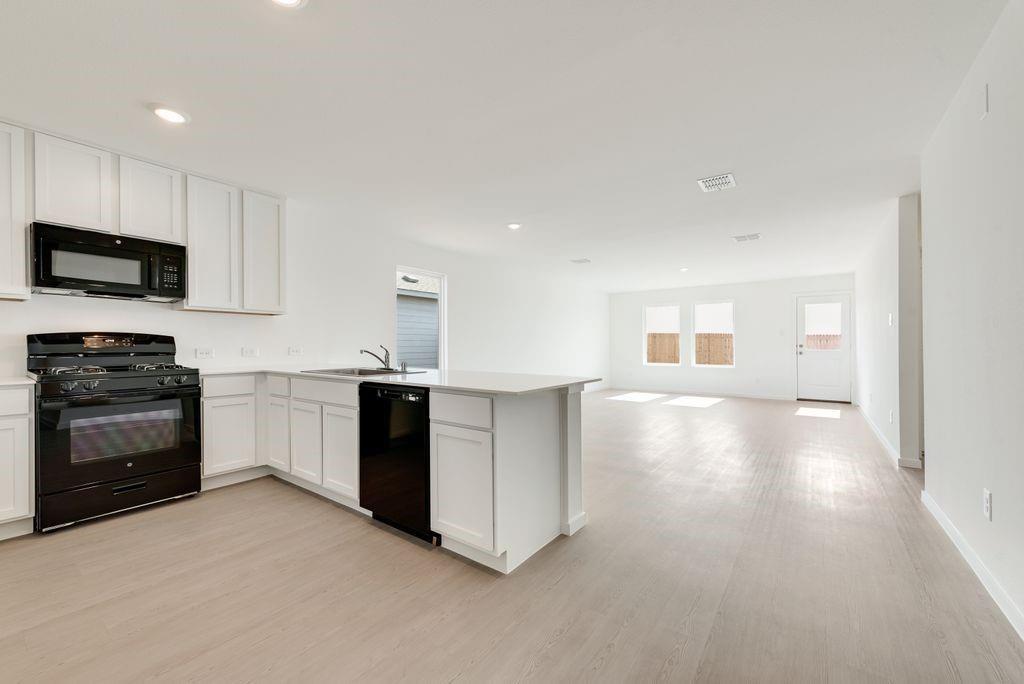 Kitchen featuring black appliances, a peninsula, light wood finished floors, open floor plan, and recessed lighting Kitchen featuring black appliances, a peninsula, light wood finished floors, open floor plan, and recessed lighting