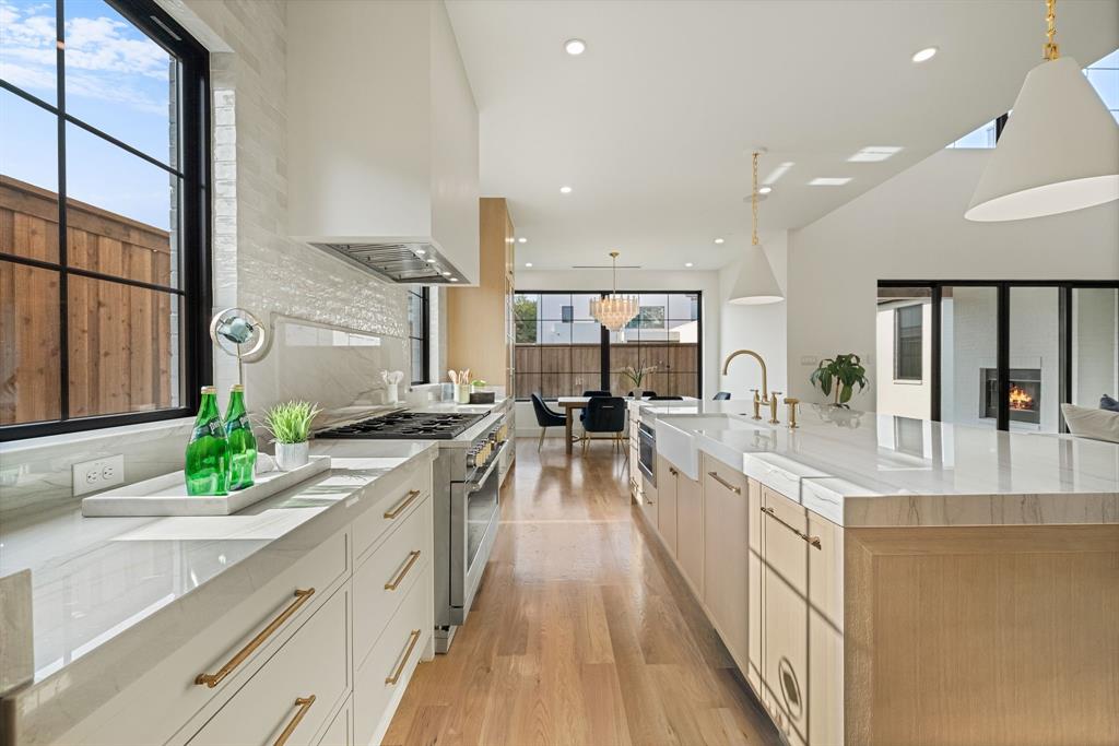 Gourmet kitchen with extensive white countertops, a large center island with a farmhouse sink, stainless steel appliances, and wood-finish flooring
