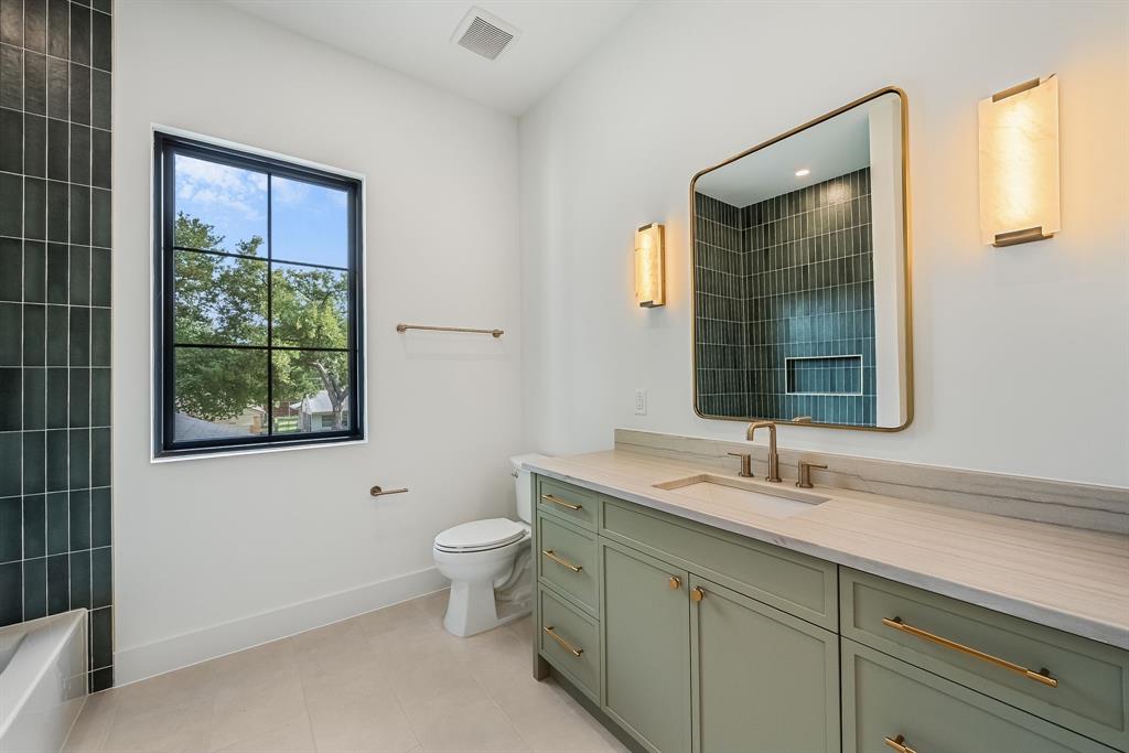 Bathroom featuring a sage green vanity with gold-tone hardware, a rectangular undermount sink, and a light-toned stone countertop