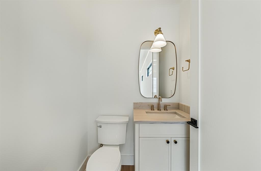 Powder room featuring a white single vanity with light-toned countertop, an integrated sink, and gold-finish hardware